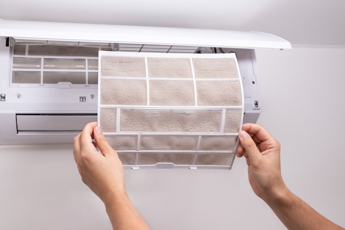 Pessoa retirando filtro sujo do ar-condicionado split para limpeza