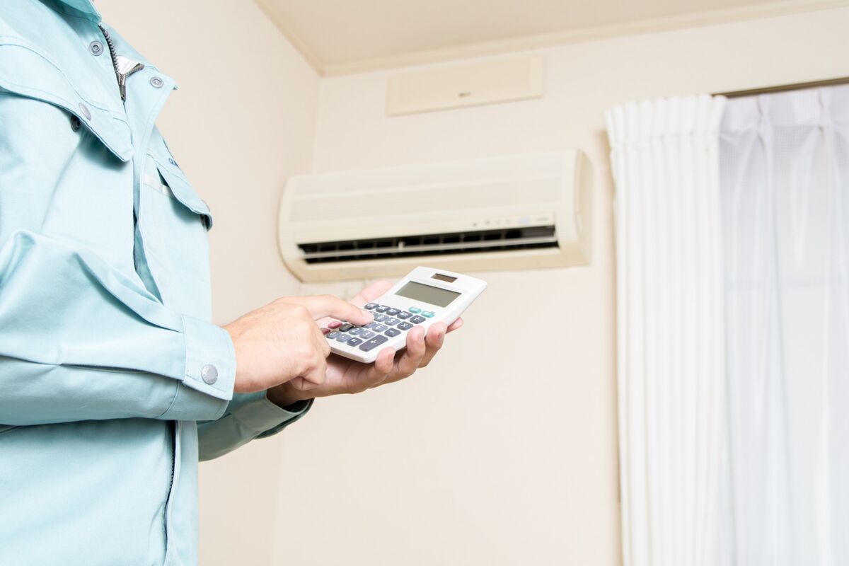 Técnico refrigerista segurando calculadora em frente a unidade interna de ar-condicionado split, avaliando causas de consumo alto