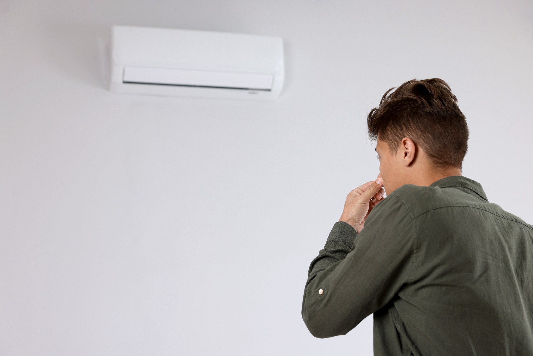 Homem olhando para ar-condicionado split na parede com expressão de preocupação com cheiro de mofo no ar-condicionado