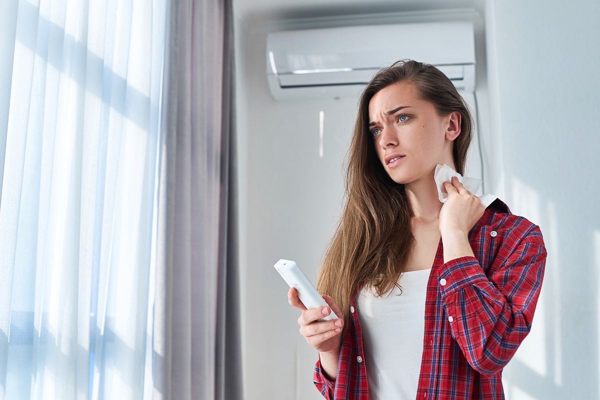 Choque térmico ar-condicionado: mulher com calor usando controle do aparelho em ambiente climatizado.