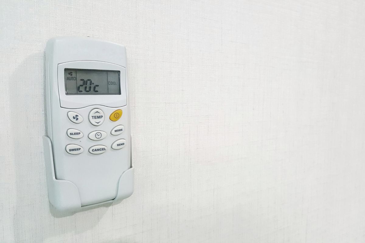 Controle remoto de ar-condicionado encaixado no suporte de parede, exibindo 20°C no visor