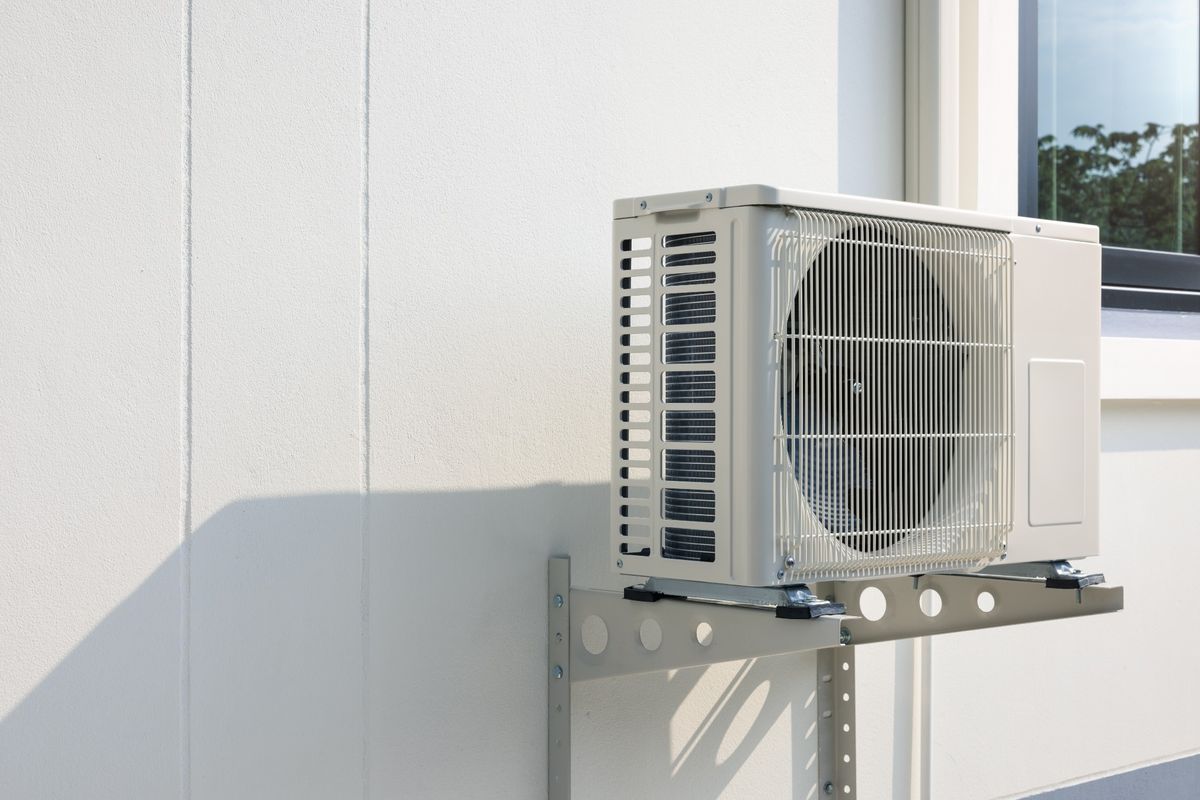 Unidade externa de ar-condicionado split instalada na parede, mostrando a serpentina e o ventilador ao lado do compressor