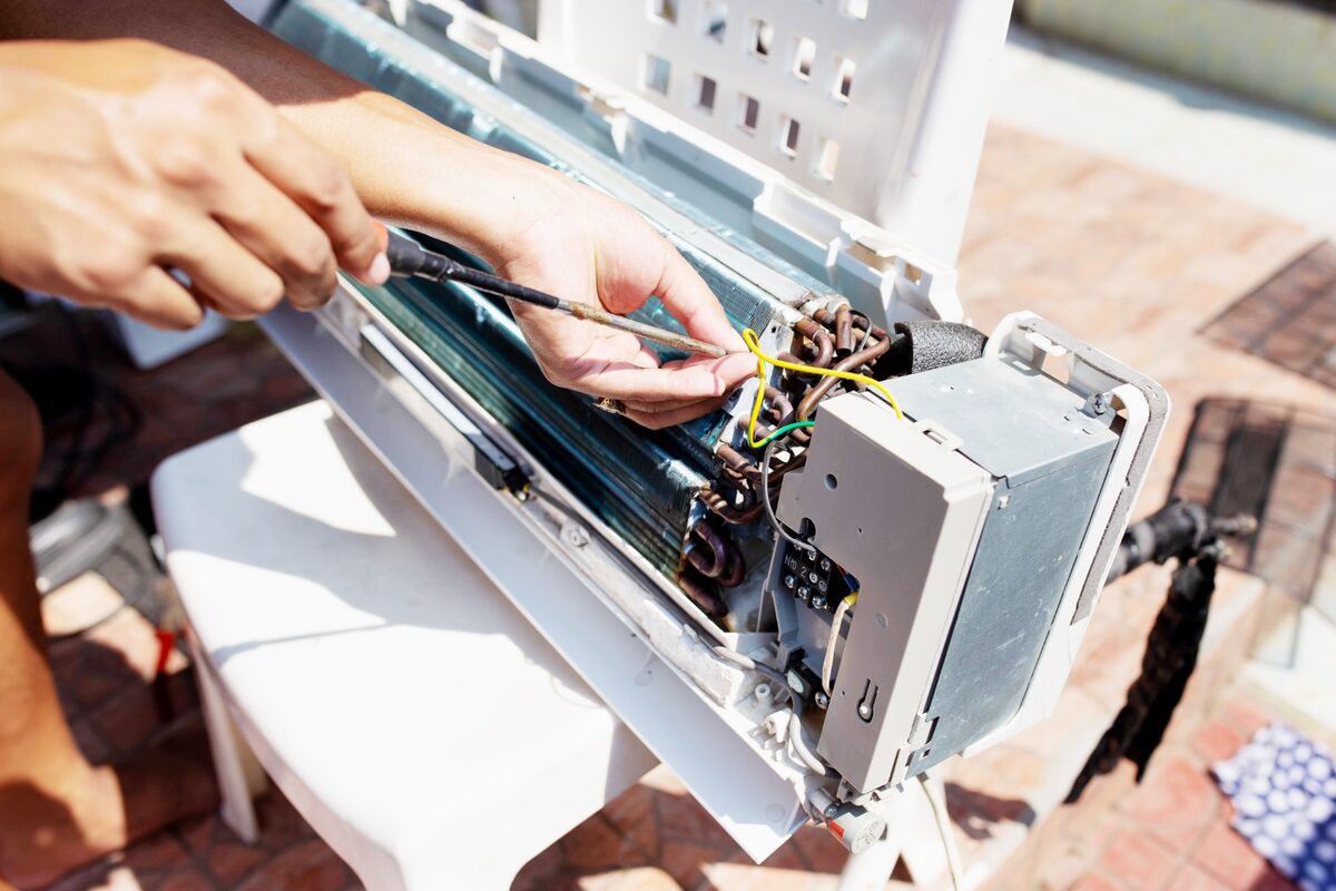 Técnico refrigerista verifica a fiação e os componentes internos de um ar-condicionado split aberto.