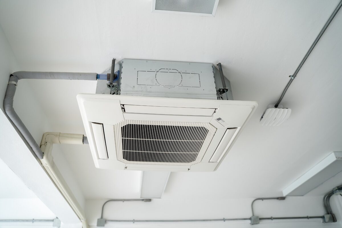 Unidade interna de ar-condicionado cassete instalada no teto com estrutura e tubulações aparentes
