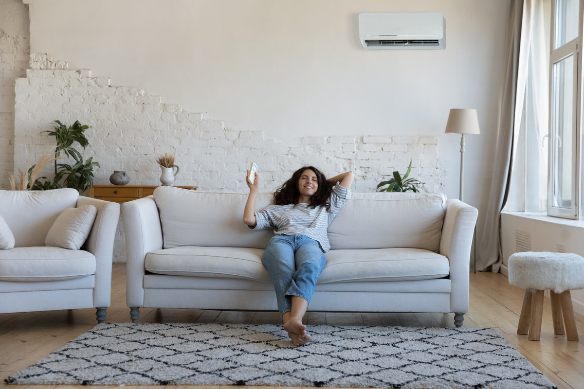 Mulher relaxando em sofá claro, com ar-condicionado split instalado na parede de uma sala iluminada.