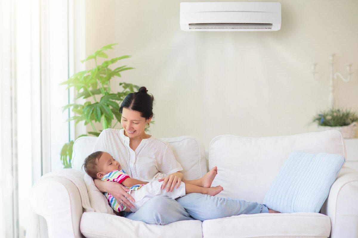 Mãe segura bebê no sofá em sala climatizada por ar-condicionado split