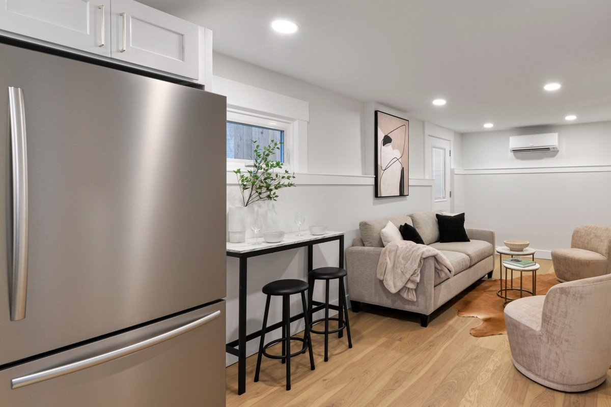 Sala com sofá, poltronas e ar-condicionado split na parede, integrada à cozinha com geladeira de inox.